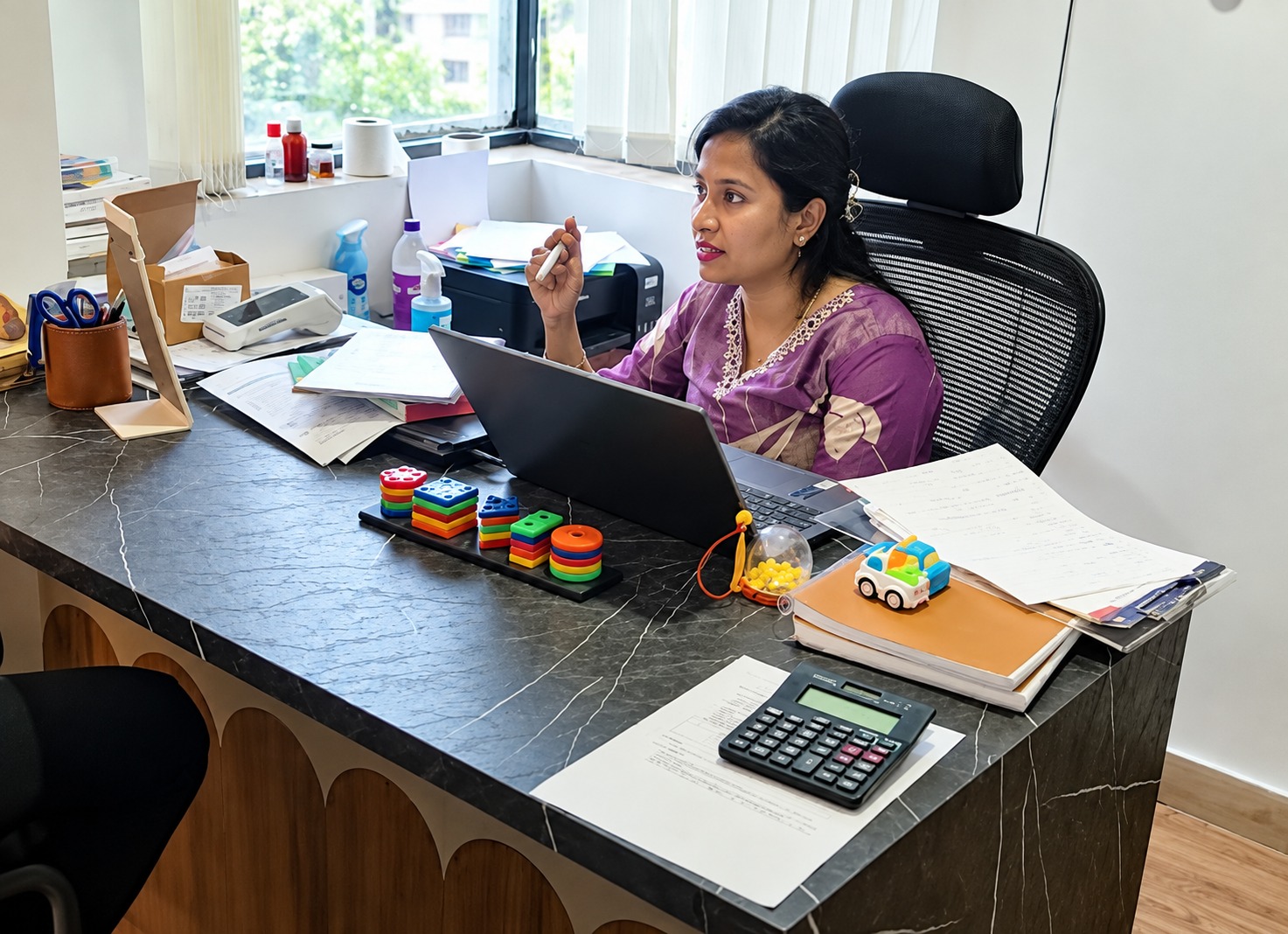 Portrait of an Indian female senior audiologist clinician Dr CS Yogashree Divakar in medical white coat with pleasant warm smile in contemporary clinic office with medical certification background in soft focus lighting.